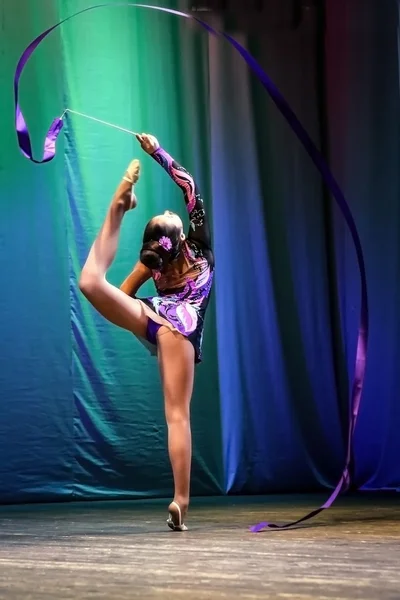 Girl on the stage performs gymnastic exercise with ribbon.