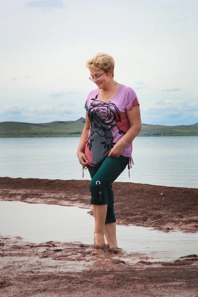 Happy adult woman in medical mud in the salty lake - rubs legs.