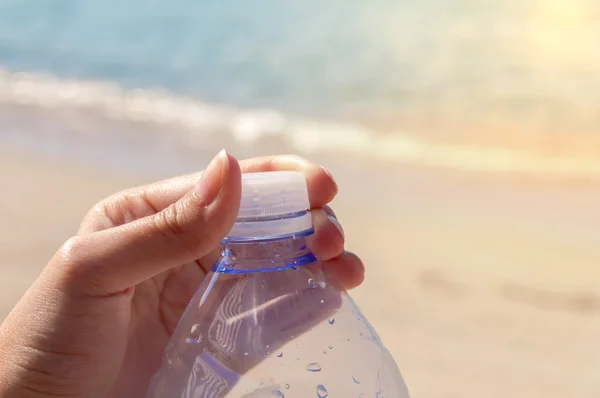 Pet bottle with water on the sea with hand closing plug on beach burning sun