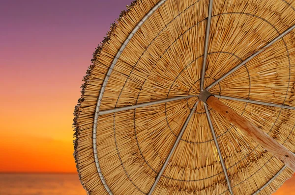 A reed sun umbrella and sun down sky symbolizing vacationing in summer