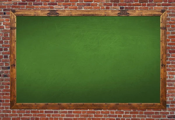 Green blackboard in wooden frame with eraser and chalk on brick wall