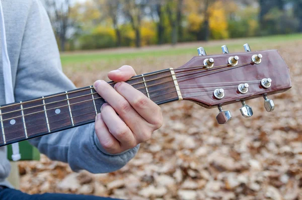 Young man holding acoustic guitar on bench in autumn park