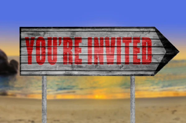 Red You\'re Invited! wooden sign with a beach on background