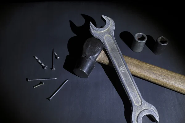 Hammer, wrench and nails on black background, light brush