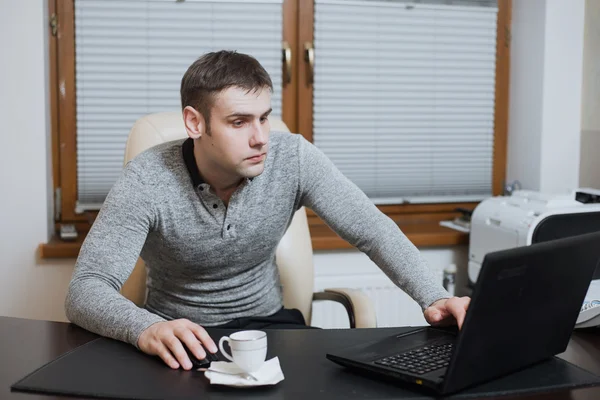 Office worker freelancer sits at the desk and working on laptop during coffee break at the office