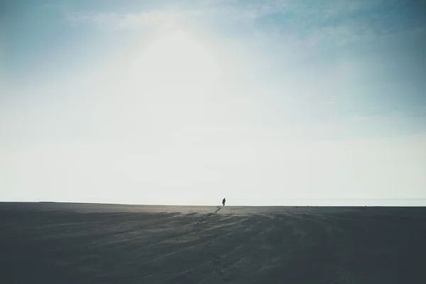 Man walking alone to horizon on black beach in Iceland leaving footprints