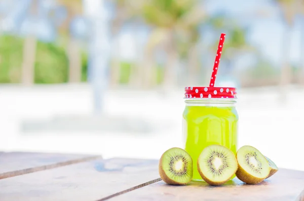 Kiwi and green juice in a glass with a straw, beach photo