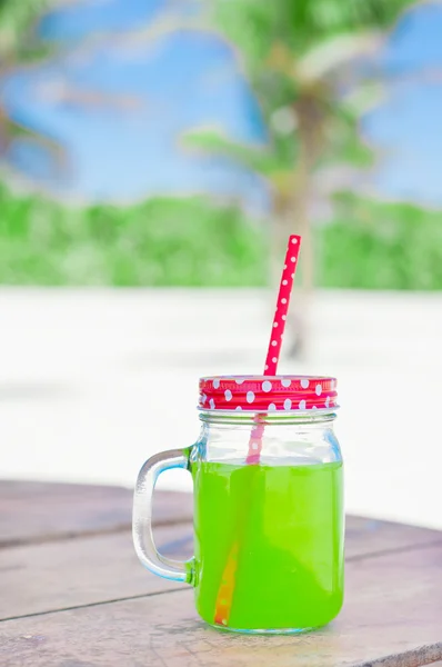 Glass with fresh green juice with red straw, palm trees