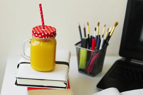 Jar with fresh orange juice standing at an office desk.
