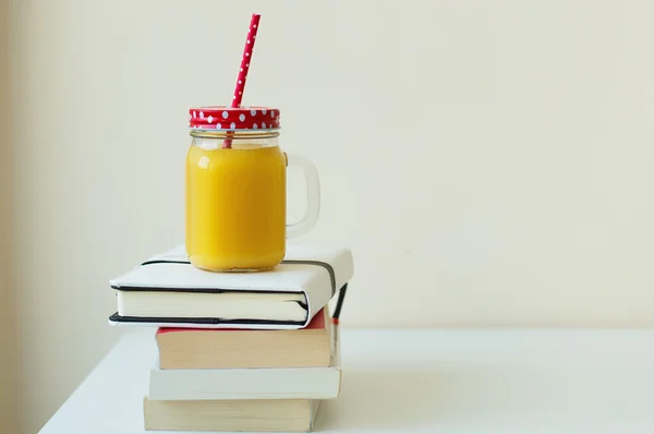 Books and orange juice in a smoothie jar with a red straw