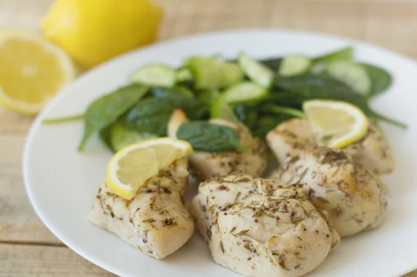 Baked chicken fillet cooked with thyme and lemon. Chicken chops served with baby spinach, cucumber and lemon on a white classic plate. Healthy eating concept