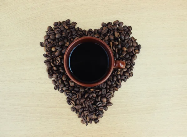 Cup of coffee and coffee beans in the form of hearts close up on a wooden background