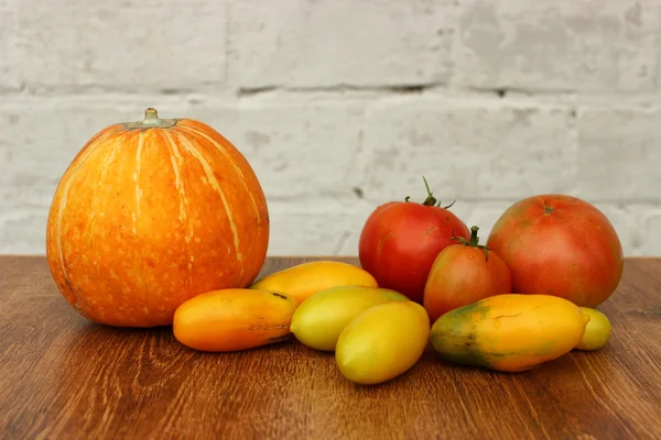 Orange pumpkin and bright multicolored tomatoes lie on a wooden table after harvest