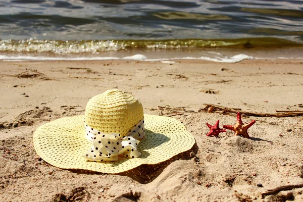 Straw hat and two red shells lie on the sand close up  a background of the sea