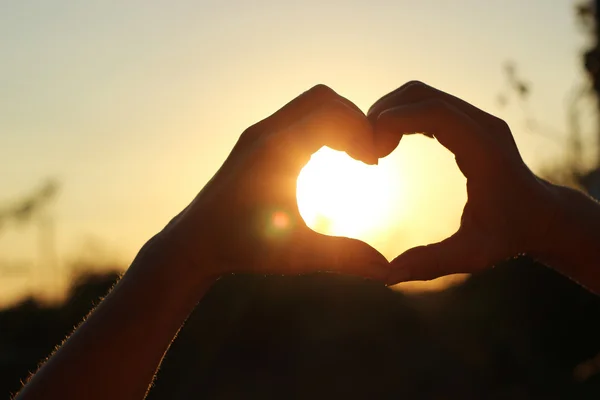 Womens hands are crossed in the form of the heart through which the sun rays make the way at the sunset