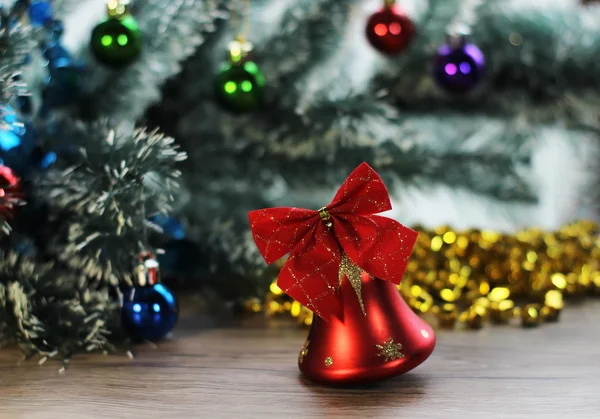 Two beautiful red shiny bells closeup on the background of Christmas tree and tinsel on the wooden floor