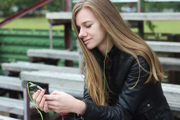 Young beautiful girl look and listening music on your mobile phone on the old stadiums bench