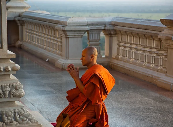 The monk kneeling at church. Young monk in a bright orange robe kneels in front of the temple with his hands clasped in prayer. December 2, 2009: The monastery.