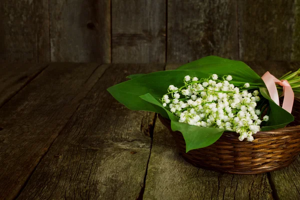 Lilies of the valley  in a basket  on the blurred old wooden bac