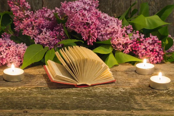Composition of the bouquet of lilac, candle and a book on the ol