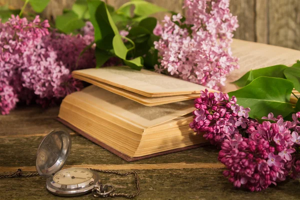 Composition of the blooming lilac branches, books and clock