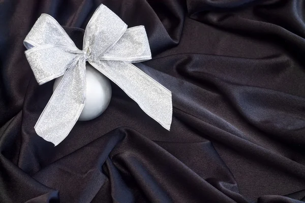 Grey Christmas ball with silver bow on black flowing fabric