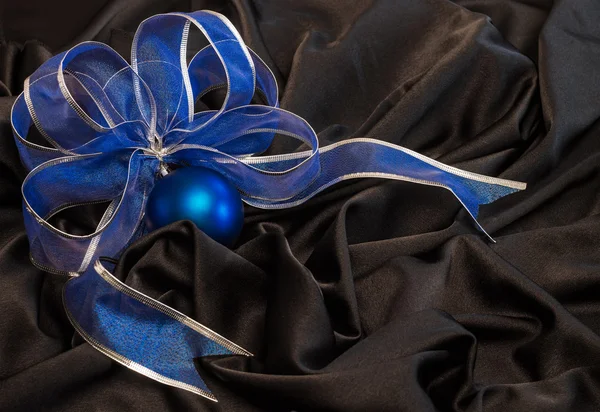 Blue Christmas ball with a blue ribbon on  black satin fabric wi