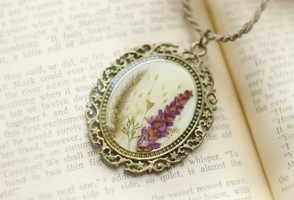 Beautiful handmade pendant with flowers in resin on open book. Woman\'s jewelry, accessory. Isolated. Close up
