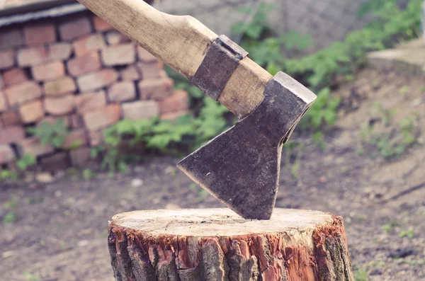 Axe carved in stump in courtyard on a brick background. Ax driven into the wood timber in the yard