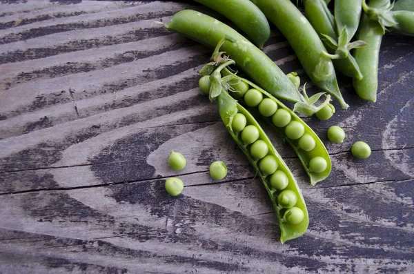 Vintage wooden surface for design with beautifully pods of green peas. Young fresh green peas on old wooden background.