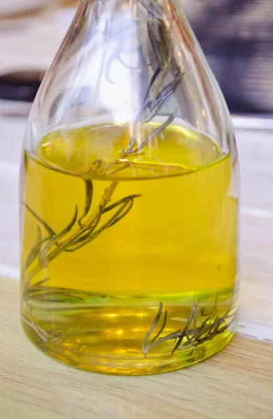 Bottle of olive oil and a sprig of rosemary inside. Transparent glass bottle on a wooden surface.