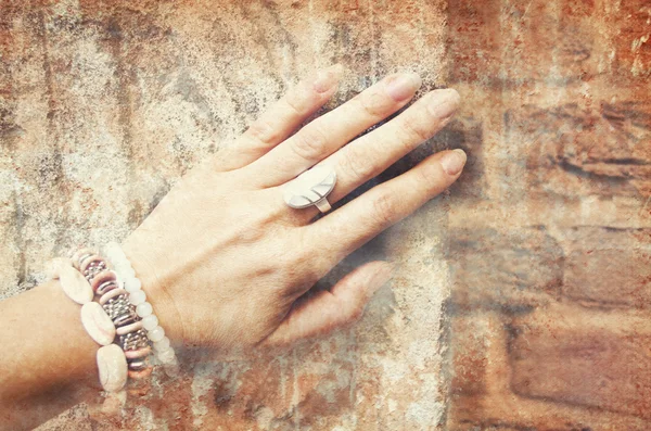 Image of beautiful female hand with ethnic ornaments on a background of ancient stone wall.