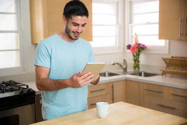 Handsome man male model with smart tablet and coffee cup in kitchen home social networking watching videos