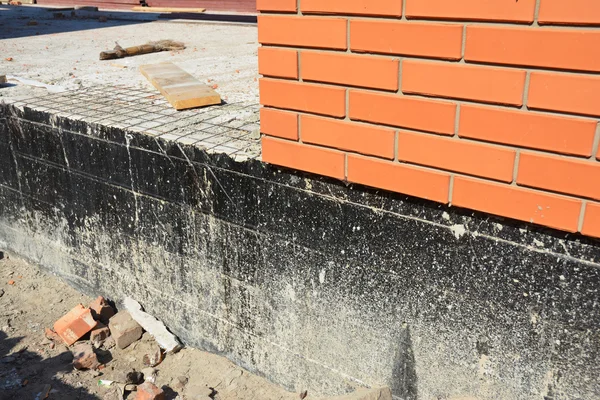 Waterproofing a new brick house foundation with spray on tar.  Construction techniques for waterproofing basements and foundations.