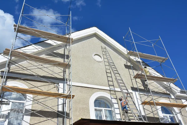 Painting and Plastering Exterior House Scaffolding Wall. Home Facade Insulation and Painting Works During Exterior Renovations. Builder Worker Plastering House Facade.