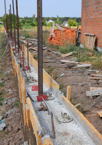 Building concrete foundation for new fence with metal supports. Construction site during concrete pouring works with formwork.