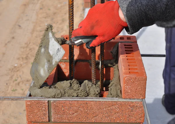 Bricklayer worker installing red blocks and caulking brick masonry joints exterior wall with trowel putty knife outdoor