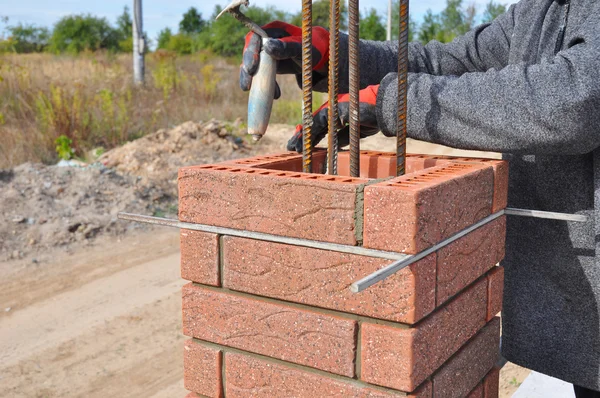 Bricklayer Worker Installing Red Clinker Blocks around Iron Bar