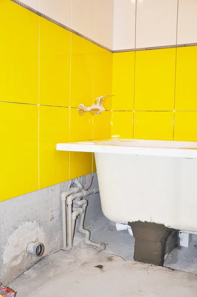 White new bath tube installation, water tap in the yellow tiled bathroom. Repair bathroom with new bath tube.