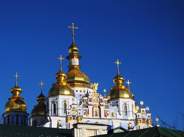 Domes and crosses of St. Michael\'s Golden-Domed Monastery in the sunset light against  blue sky. Kiev, Ukraine