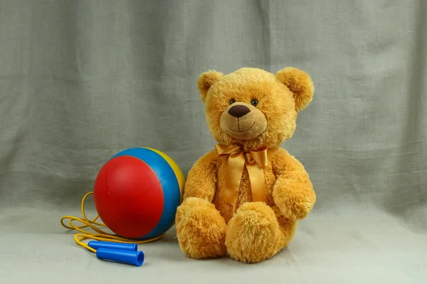 Smiling orange toy bear with a striped ball and rope