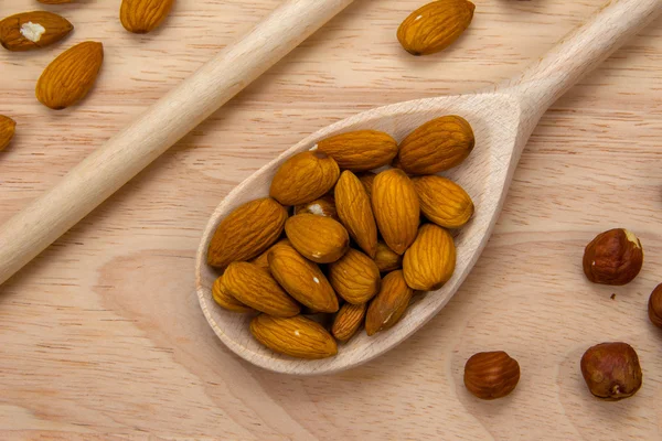Almonds in wooden spoon on wooden board