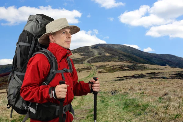 Equipped with traveler in a red jacket with Hiking poles looks i