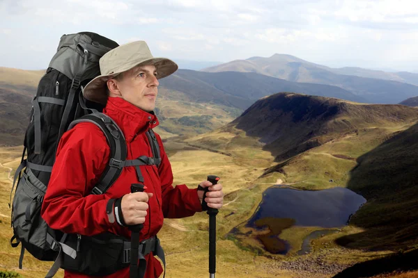 Equipped with traveler in a red jacket with Hiking poles looks i