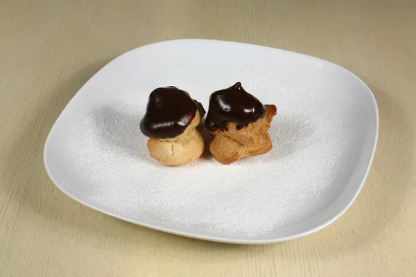 Profiteroles with chocolate icing on a plate with powdered sugar