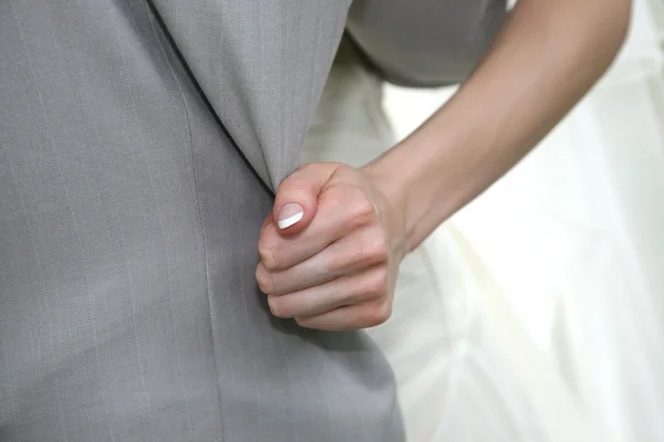 Bride holds the hand over the edge of the groom's suit