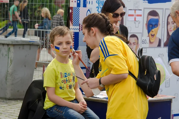 Football volunteer is drawing the flag of Ukraine on cheeks of a boy.