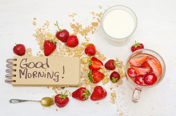 Good morning note in a notebook with craft brown pages, ripe strawberries, milk and oat muesli for breakfast