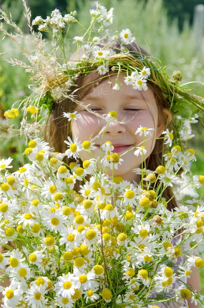 Little happy girl in a garland of field flowers in the meadow