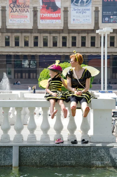 Kharkiv, Ukraine - June 18, 2016: Mother and daughter dreessed in costumes of bees are drying their feet after washing them in the fountain. Costumed bike ride \